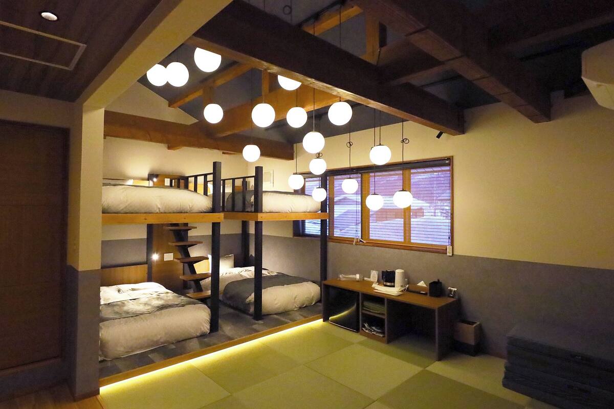A dormitory room with bunk beds, a desk, and a window with blinds.