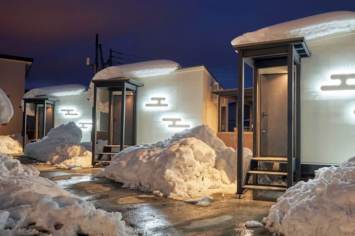 A row of small, snow-covered buildings with illuminated signage, surrounded by large snow piles.