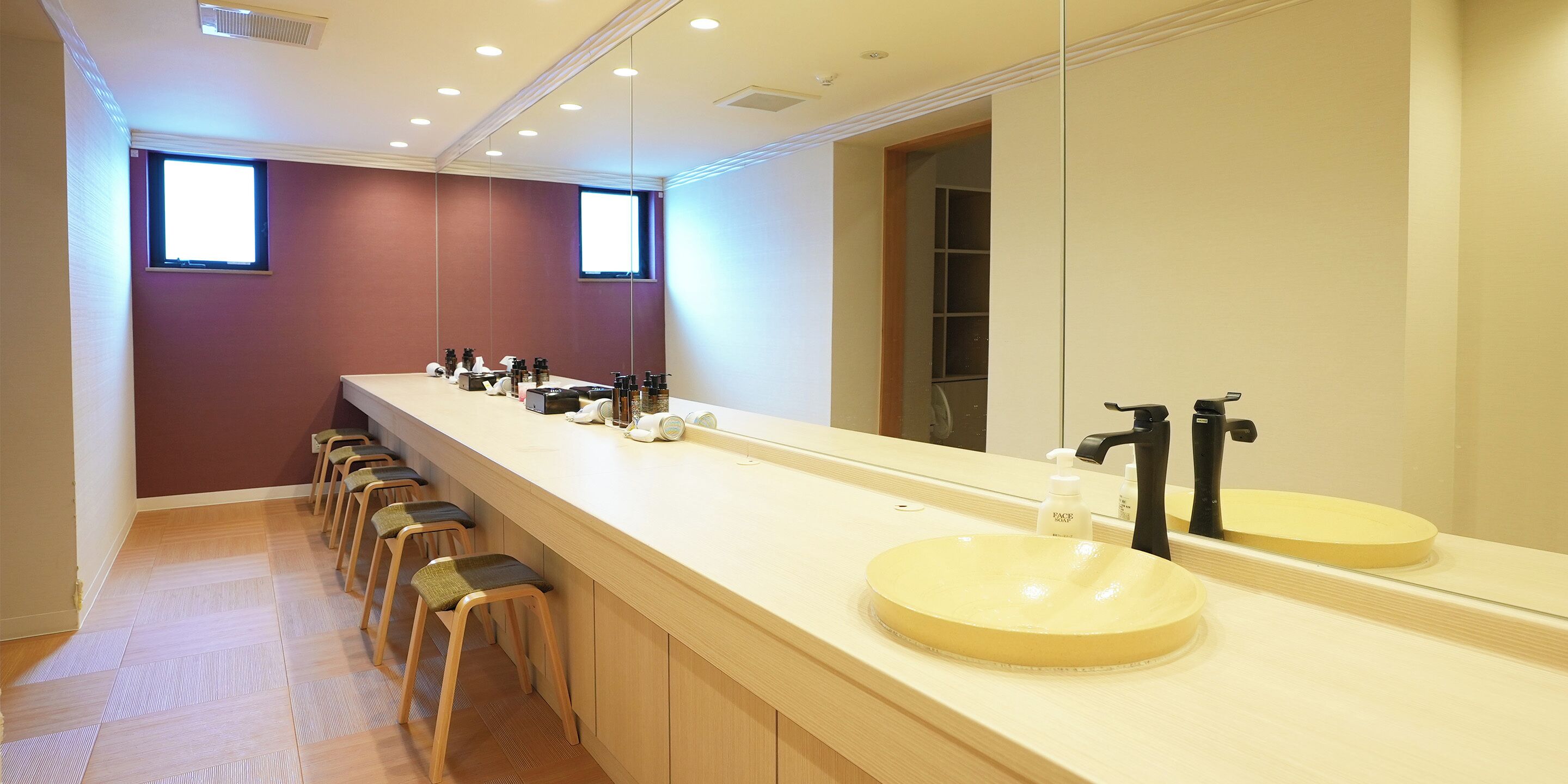 A long, narrow bathroom with two sinks, a large mirror, and a row of stools.