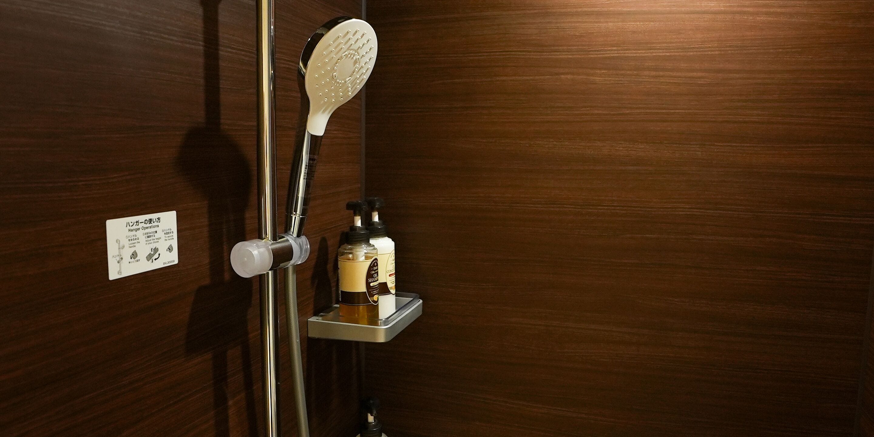 A shower with a handheld showerhead and a bottle of shampoo on a shelf.