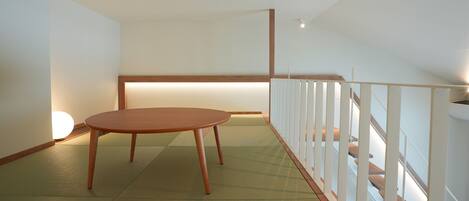 Une pièce avec un sol recouvert de tatamis, une table en bois et une rambarde basse en bois.