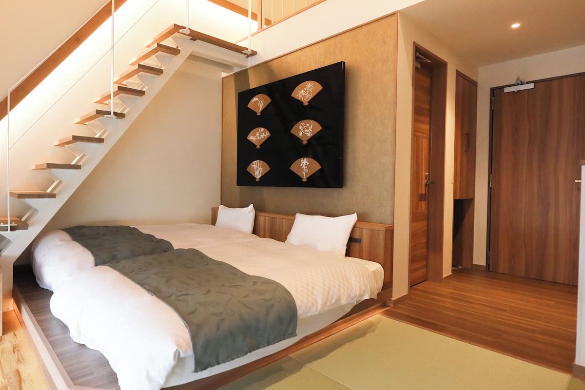 A bedroom with a large bed, a wooden staircase, and a wall-mounted artwork.