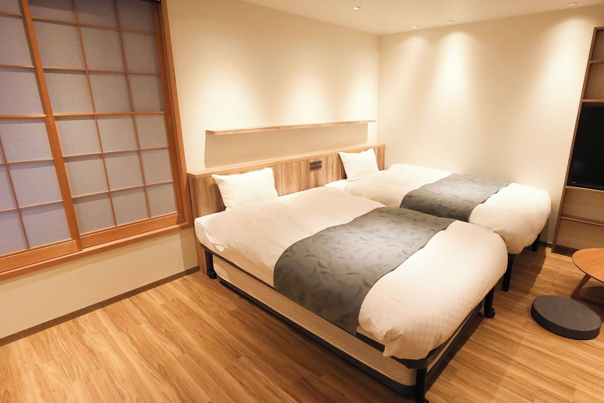 A modern hotel room with two beds, a TV, and a small wooden table.