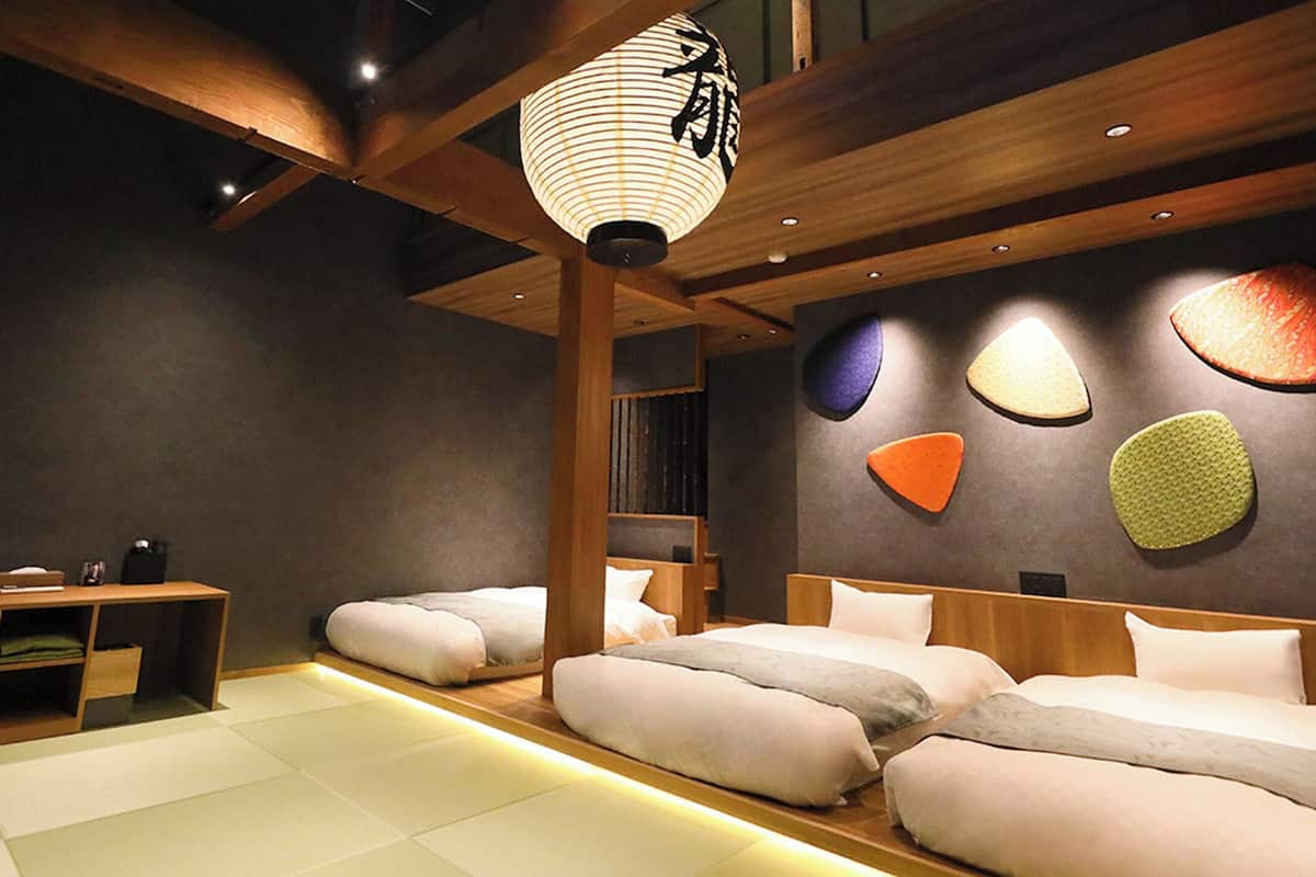 A modern hotel room with a large bed, a small desk, and a traditional Japanese lantern.
