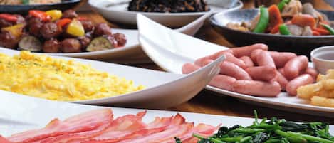 A variety of dishes including scrambled eggs, bacon, sausages, and vegetables on a table.
