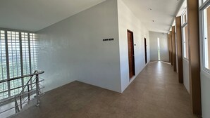 Un pasillo largo y estrecho con barandilla metálica a la izquierda, puertas de madera a la derecha y un cartel que indica los números de habitación B309-B310.