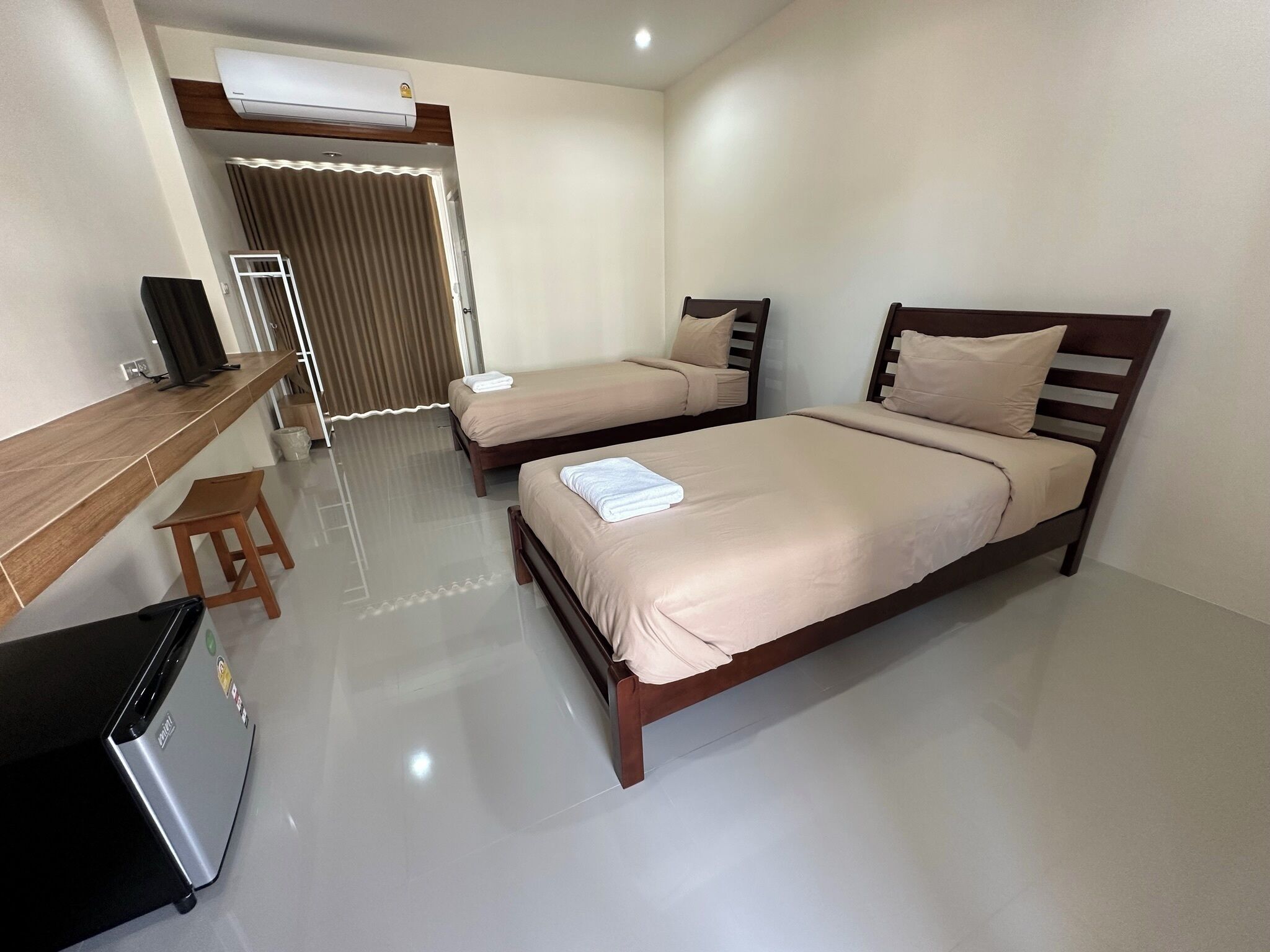 A hotel room with two beds, a desk, a chair, and a refrigerator.