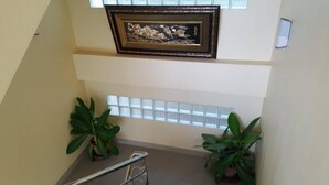 Una escalera flanqueada por plantas en macetas, con una obra de arte enmarcada arriba y una ventana con persianas.