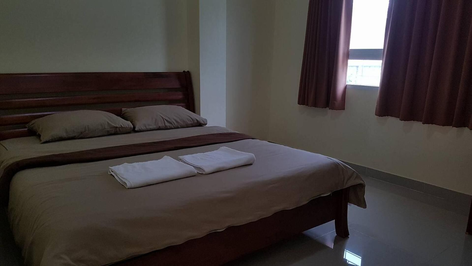 Una cama bien hecha con cabecera de madera, un par de toallas dobladas y una ventana con cortinas.