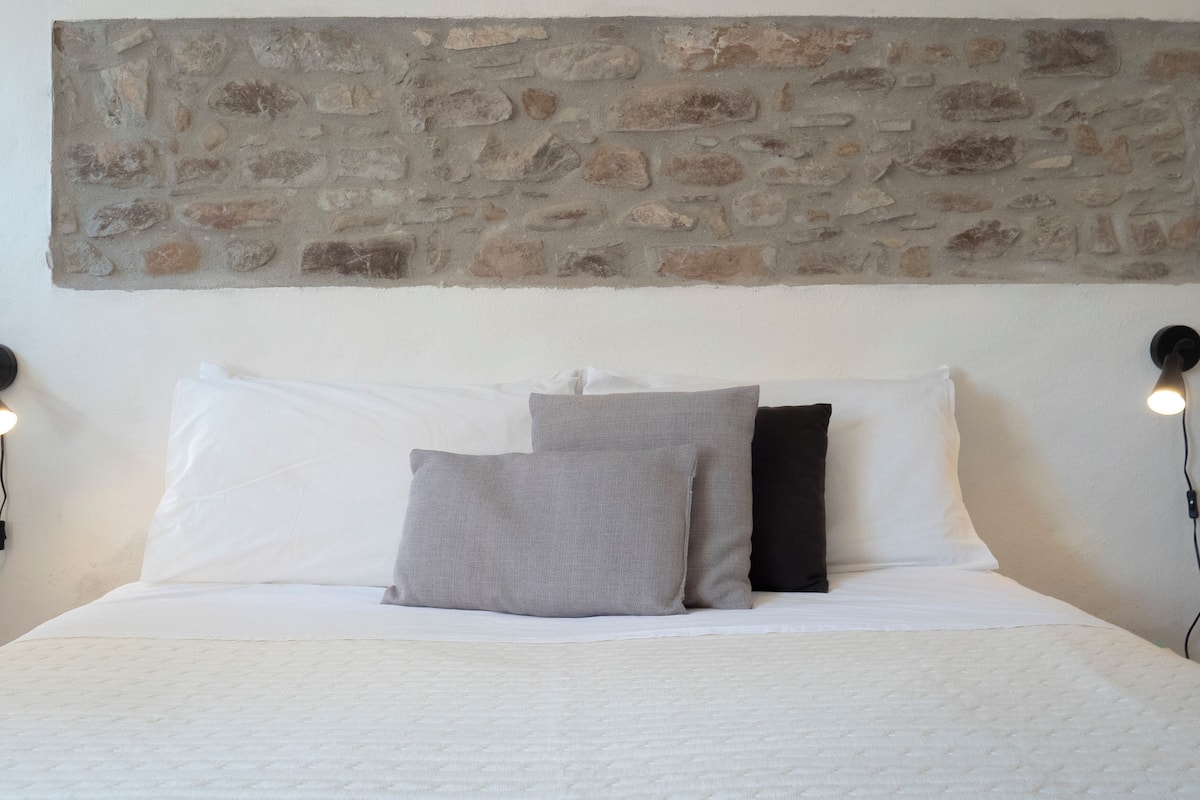 A bed with white bedding, two pillows, and a stone wall above.