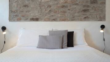 Ein Bett mit weißer Bettwäsche, zwei Kissen und eine Steinwand darüber.