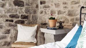 A bed with white and blue pillows, a small table with a book titled "Street Art" and a potted plant, and a stone wall in the background. - Ca'Luni (Casola in Lunigiana)