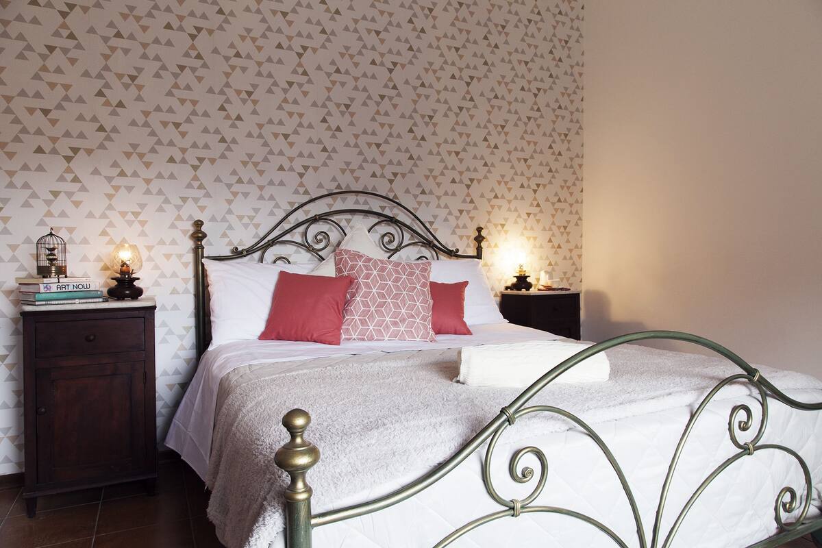 A neatly made bed with a metal headboard, a bedside table with a lamp, and a wall with a geometric pattern.