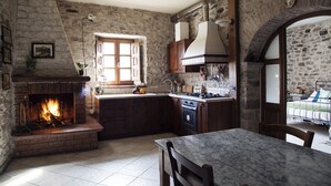 A rustic kitchen with a brick fireplace, wooden cabinets, and a stone wall. - Ca'Luni (Casola in Lunigiana)