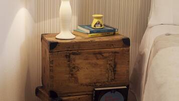 A wooden nightstand with a white lamp, a small yellow candle, and a few books.