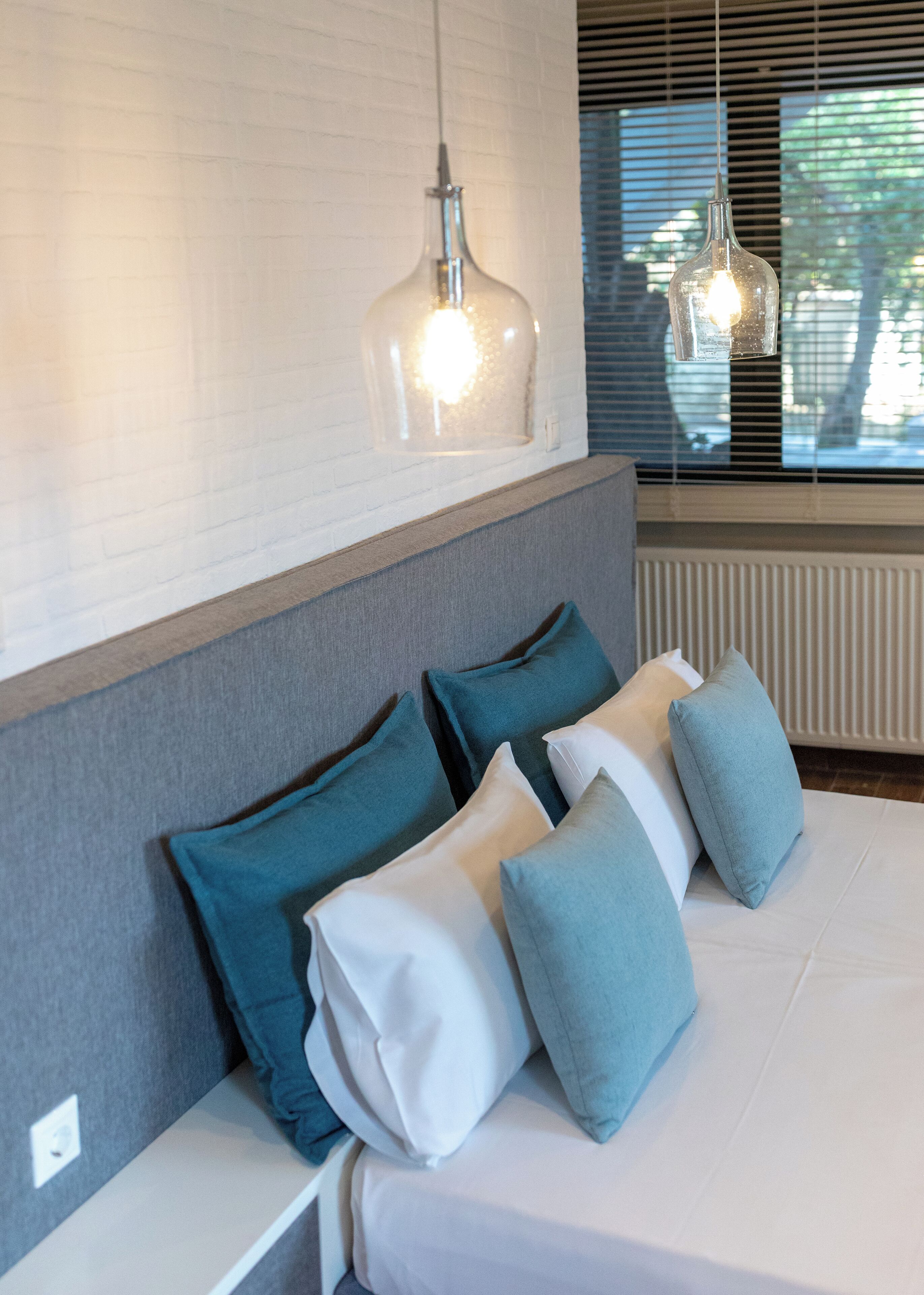 Un dormitorio moderno con cabecera gris, ropa de cama blanca y almohadas verde azulado y blancas.