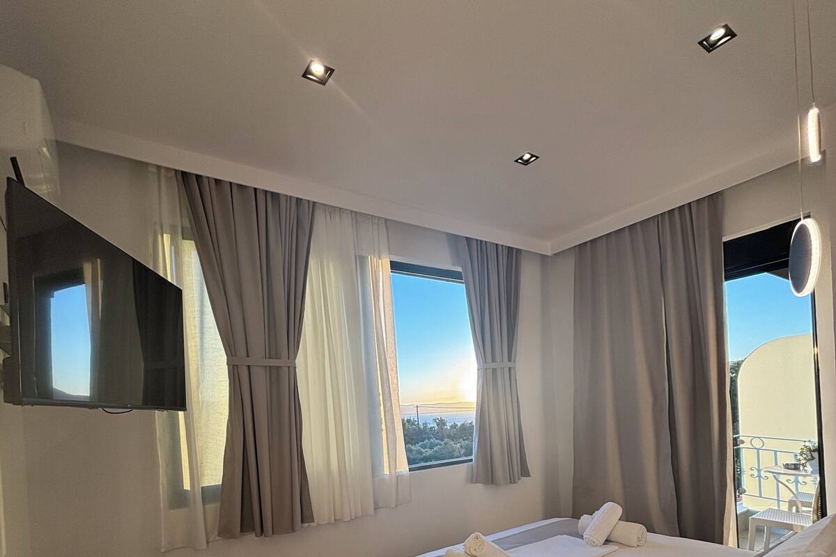 Una habitación de hotel moderna con una cama grande, un televisor en la pared, una silla y vistas al balcón.