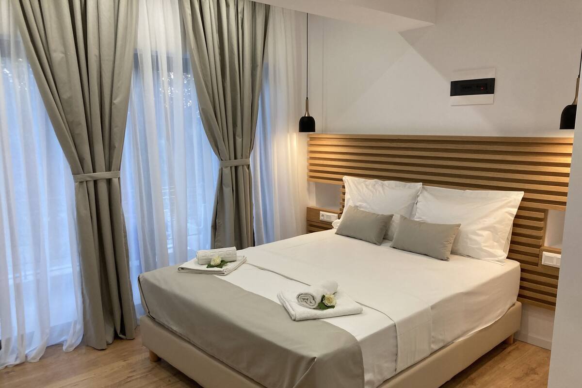Una cama bien hecha con cabecera de madera, una mesita de noche y una ventana con cortinas de encaje.
