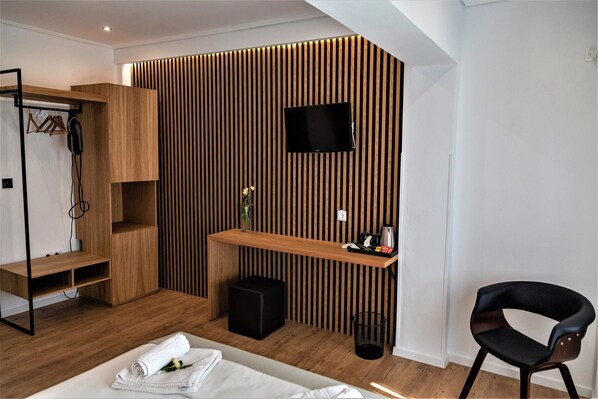 A modern room with a wooden slatted wall, a flat-screen TV, a wooden desk, a black chair, and a bed with neatly folded white towels. - Ampoulos Rooms & Apartments (Lesvos)
