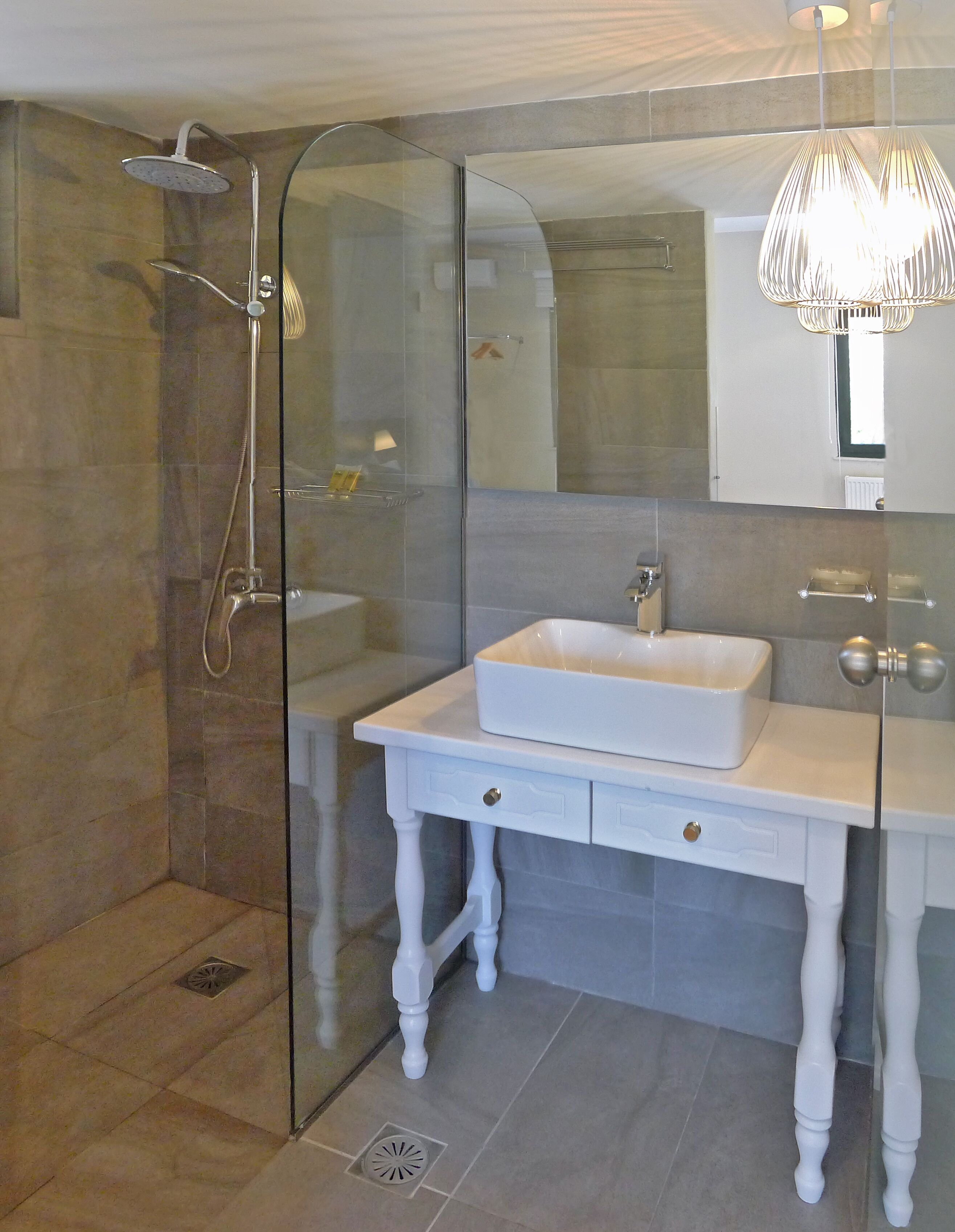 A modern bathroom with a glass-enclosed shower, a white vanity with a rectangular sink, and a large mirror.