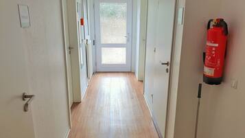 Un couloir avec un extincteur fixé au mur, une porte au fond et une pancarte au-dessus de la porte.