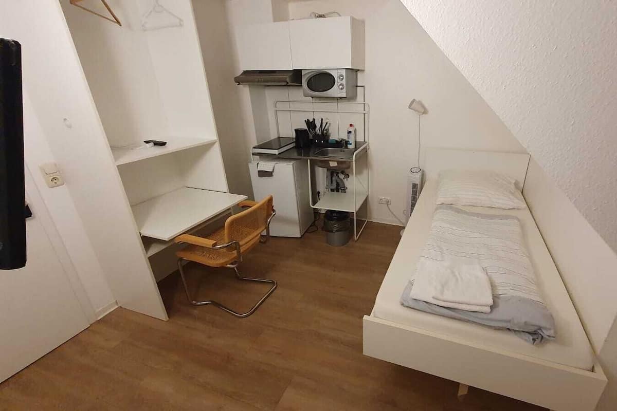 A small, compact room with a bed, a desk, and a kitchenette.