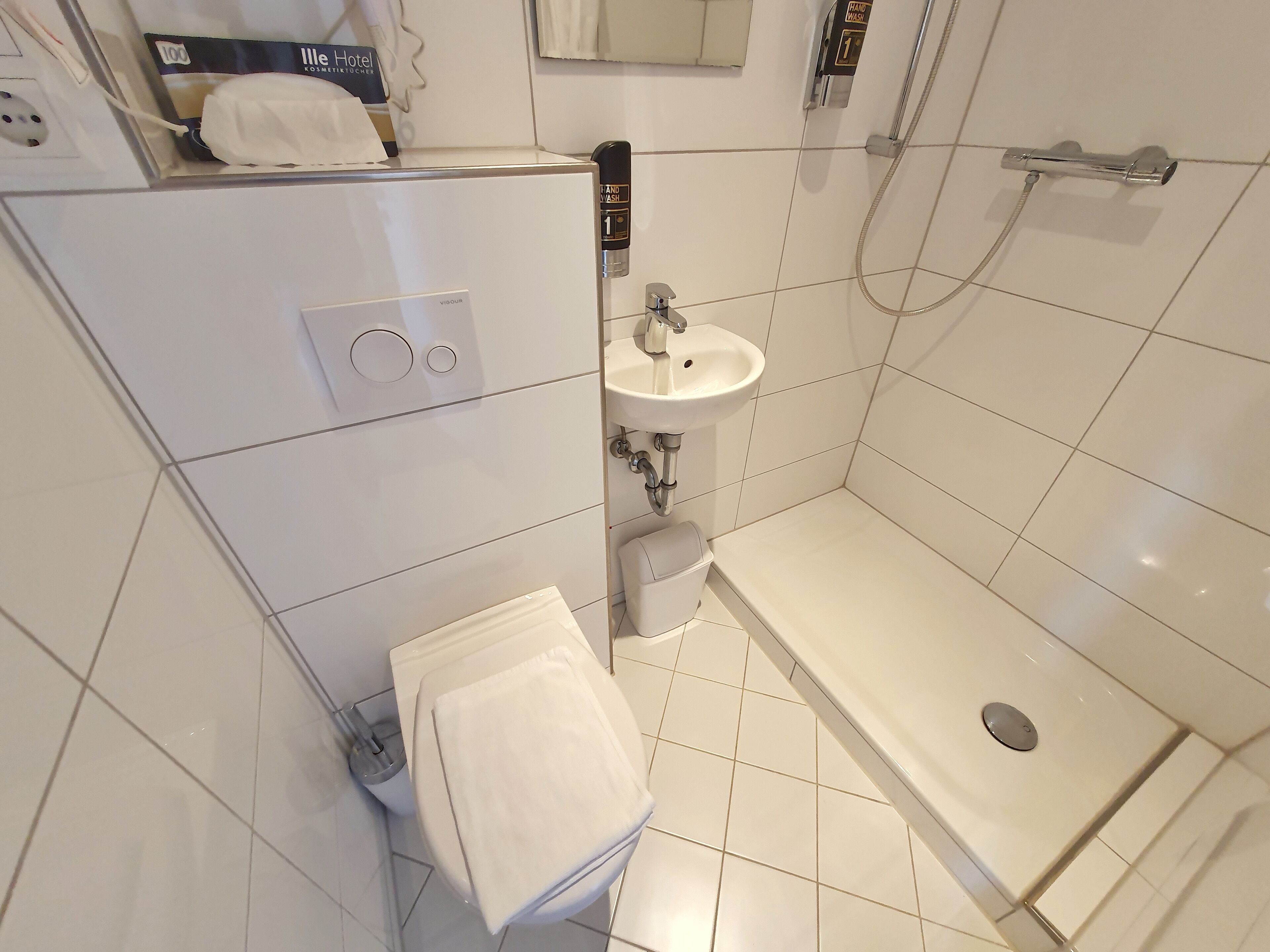 Et lille badeværelse med toilet, håndvask og bruser.