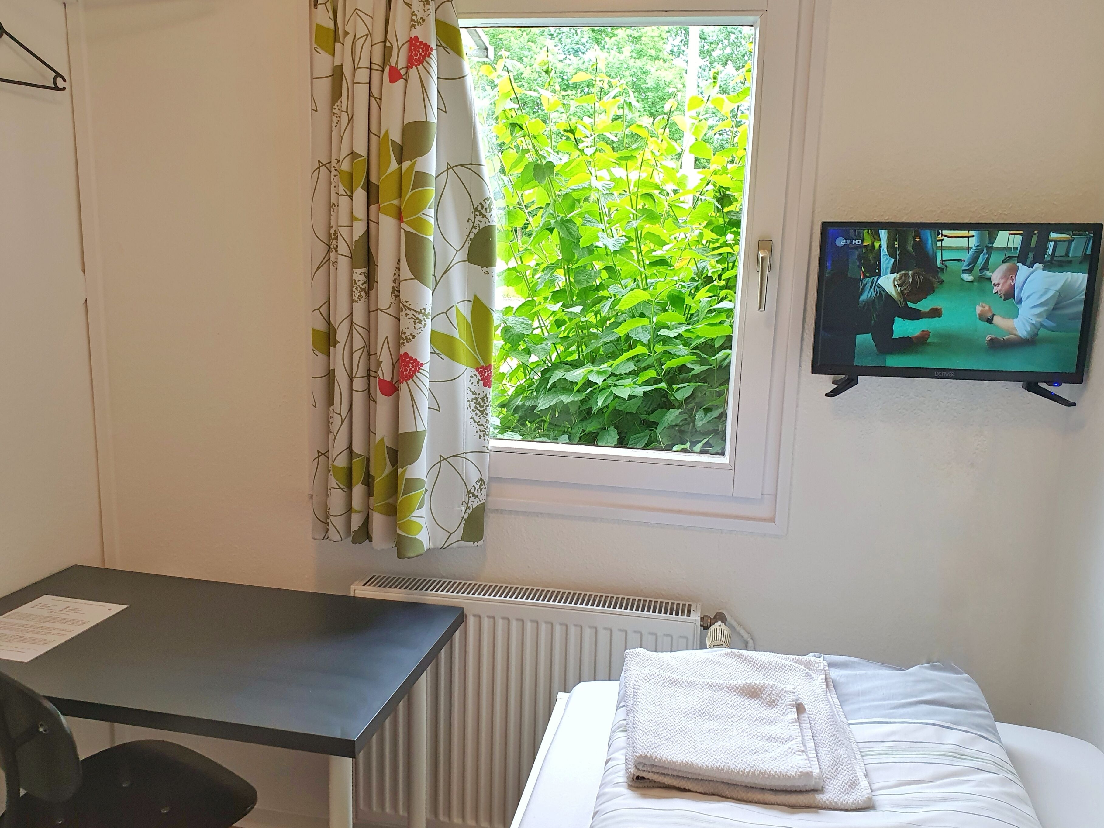 Une chambre d’hôtel avec un lit, un bureau, un radiateur et une fenêtre avec des rideaux.