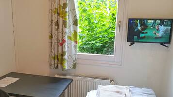 Une chambre d’hôtel avec un lit, un bureau, un radiateur et une fenêtre avec des rideaux.