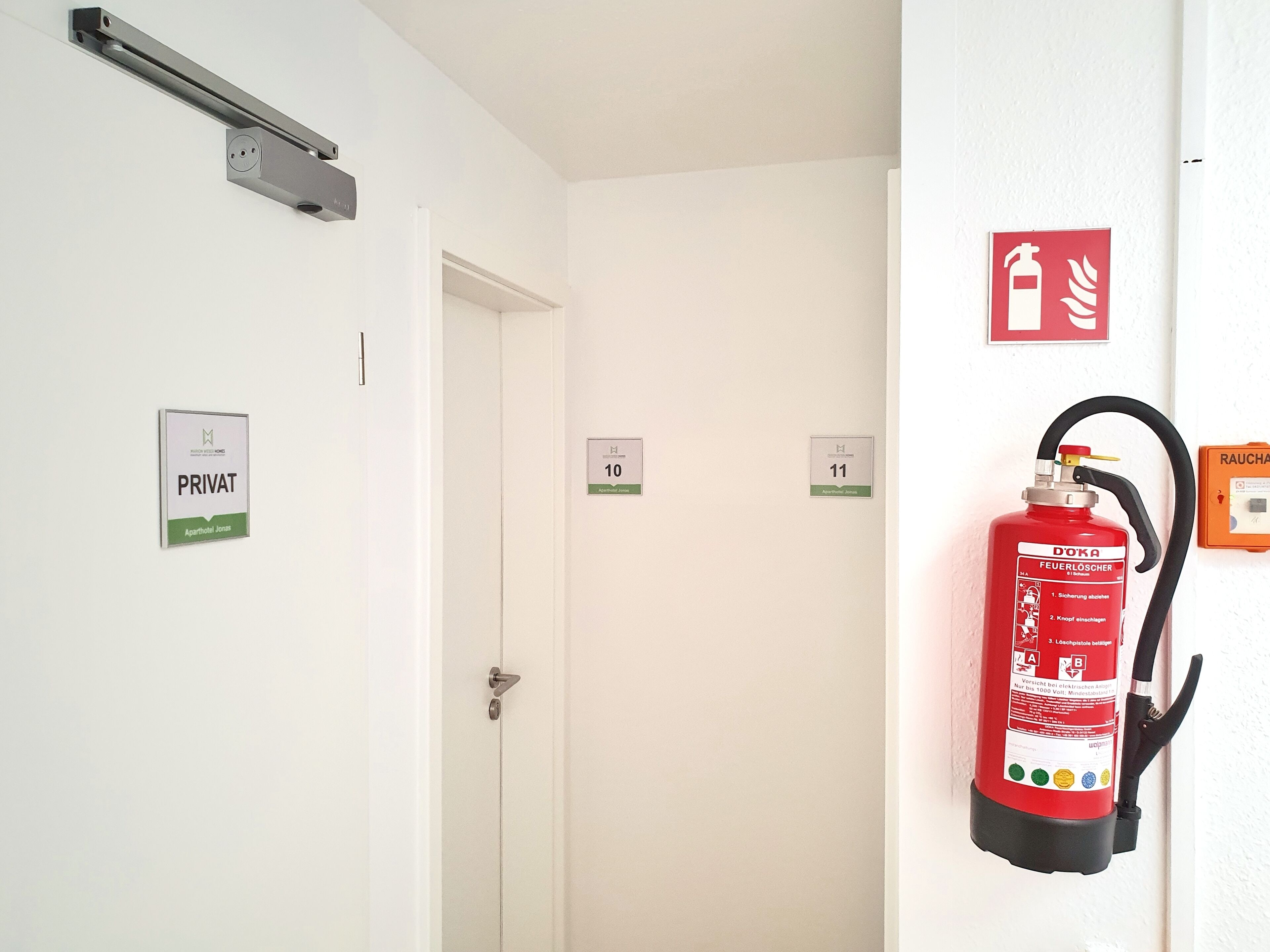 Un pasillo con puertas identificadas con los números 10 y 11, un extintor de incendios montado en la pared, y un letrero que indica zona privada.