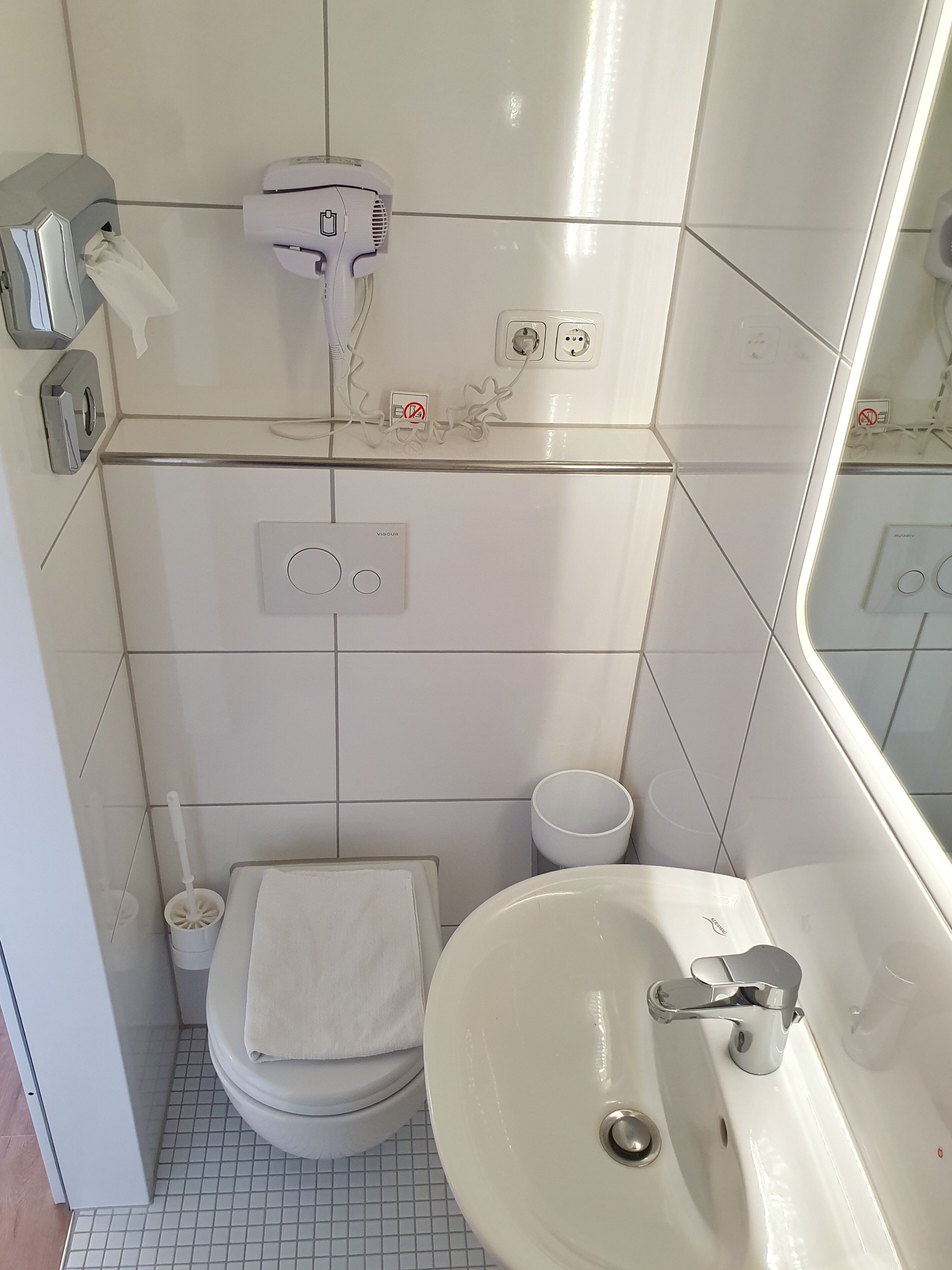A small bathroom with a toilet, a sink, a towel, a hairdryer, and a mirror.