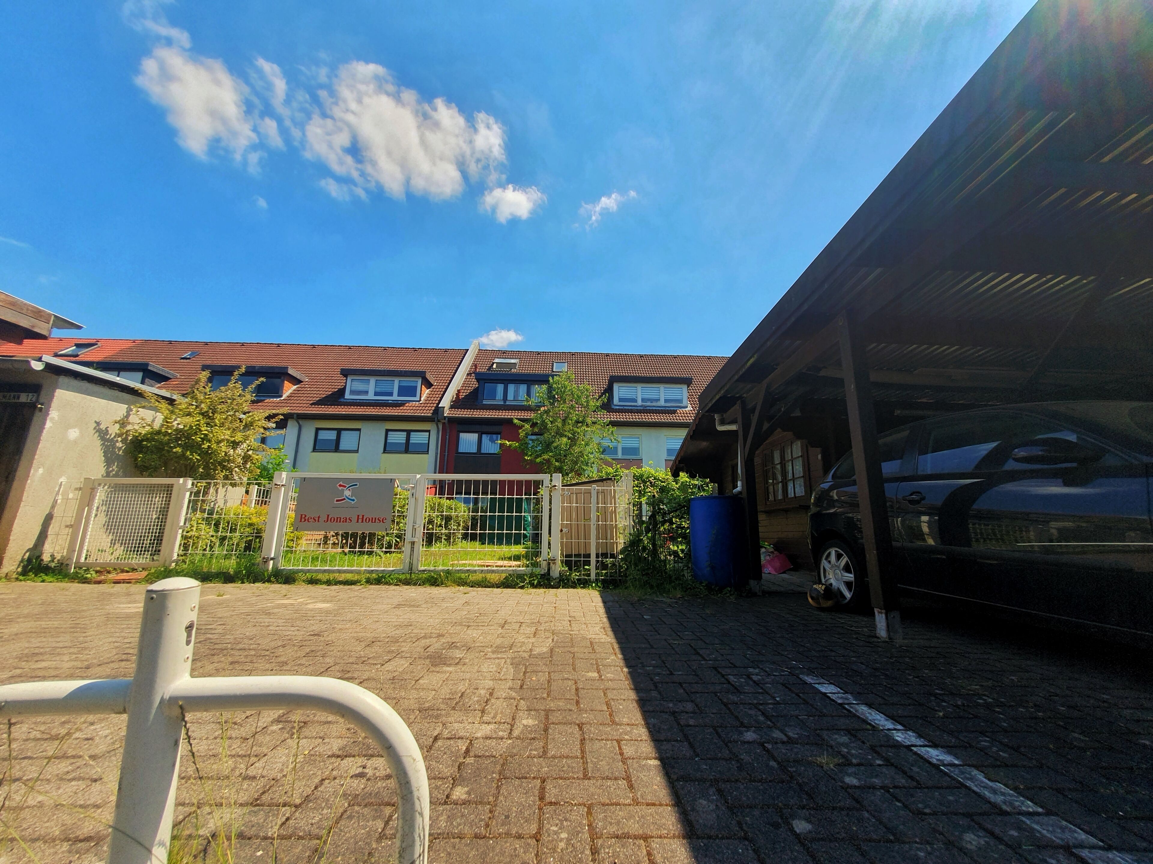 Un'area di parcheggio con un carportal coperto, un ingresso con cancello e un edificio con numerose finestre e balconi.