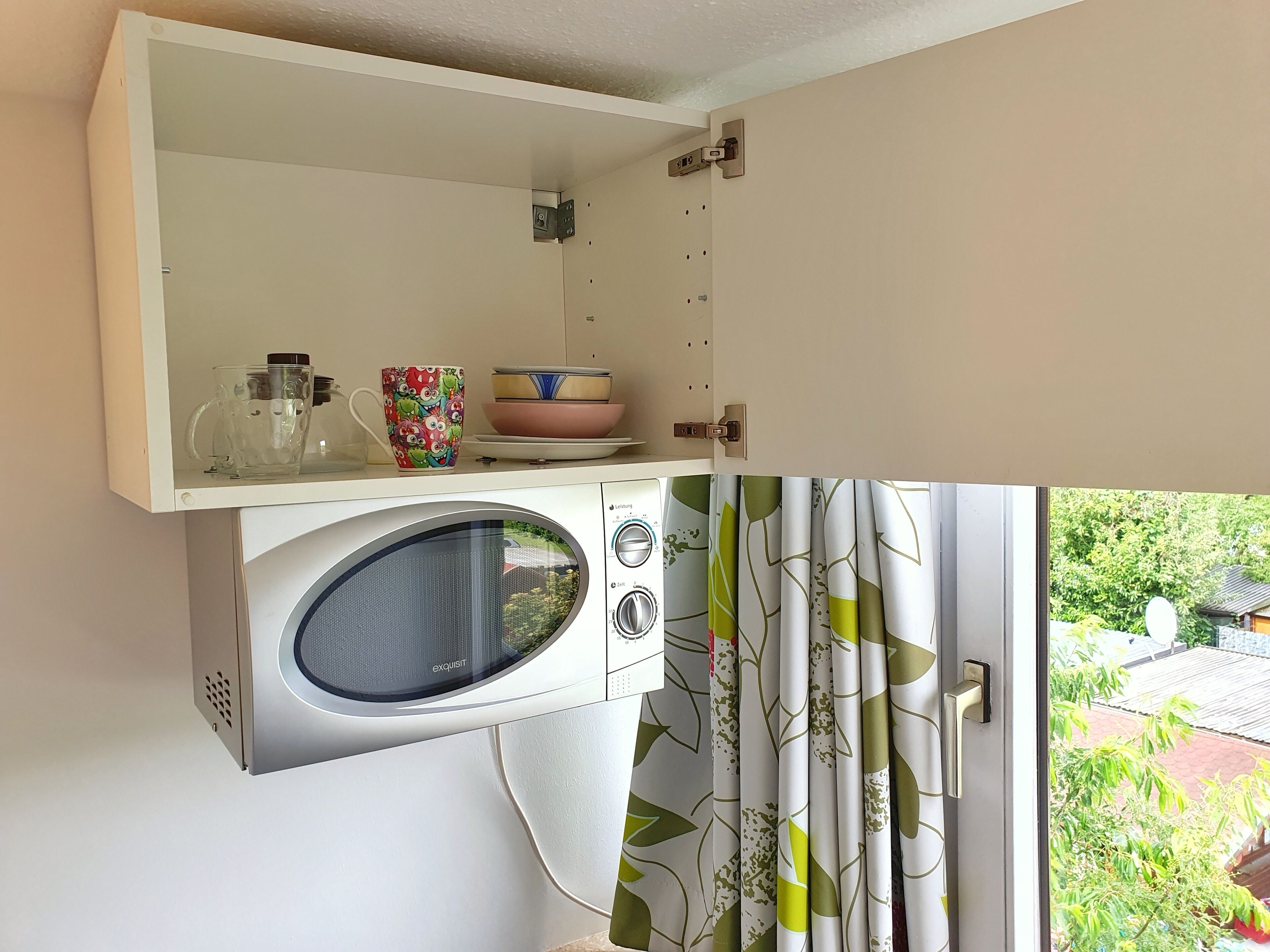 Una cocina compacta con lavadora integrada, un estante pequeño con utensilios de cocina y vistas al jardín por la ventana.