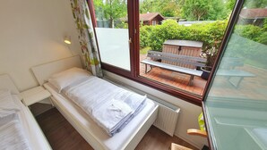 A small, single-bed room with a window overlooking a garden and a wooden bench. - Aparthotel Jonas (Bremen)