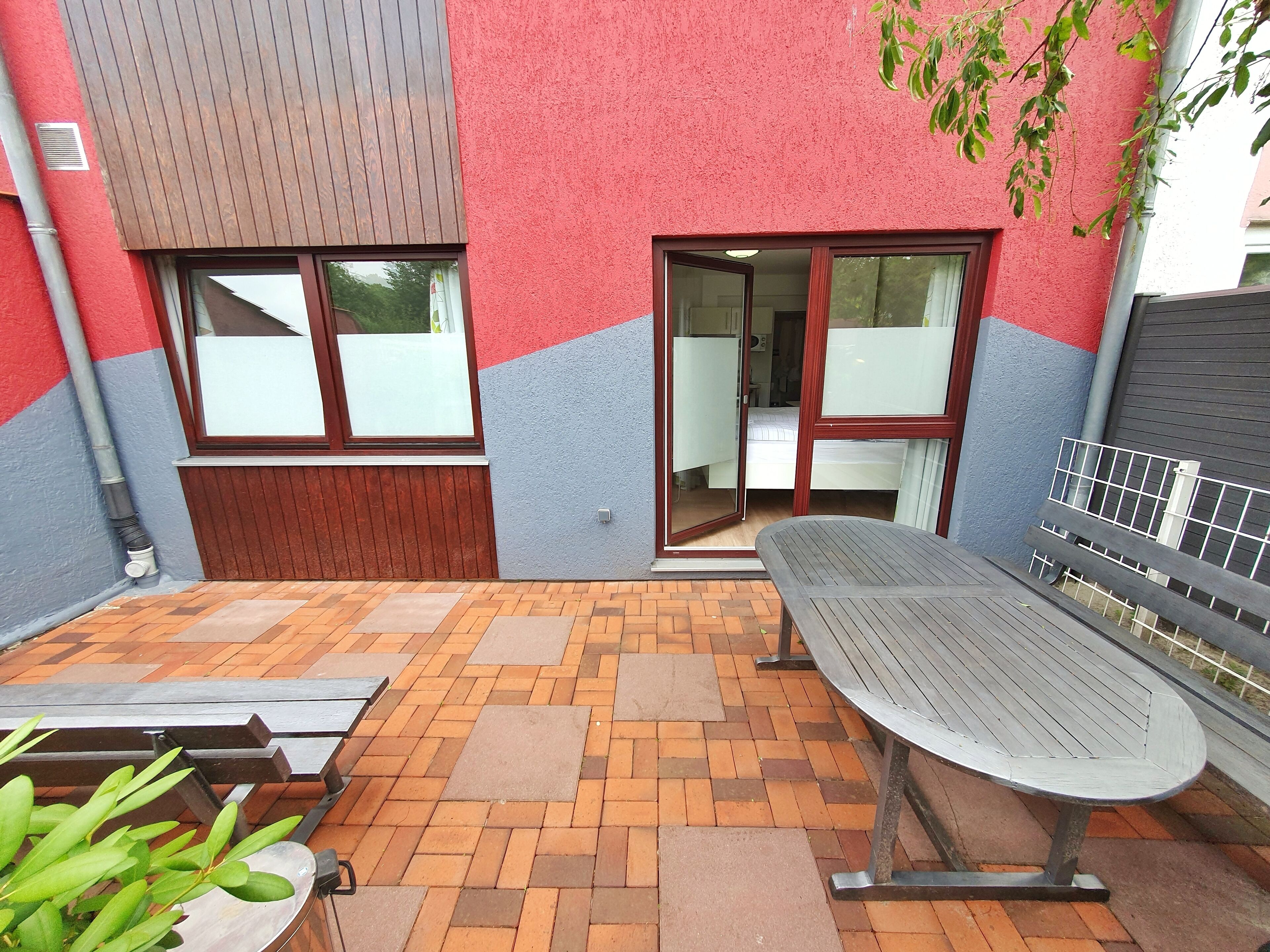 A patio area with a table and benches, a sliding glass door leading to a room, and a brick floor.