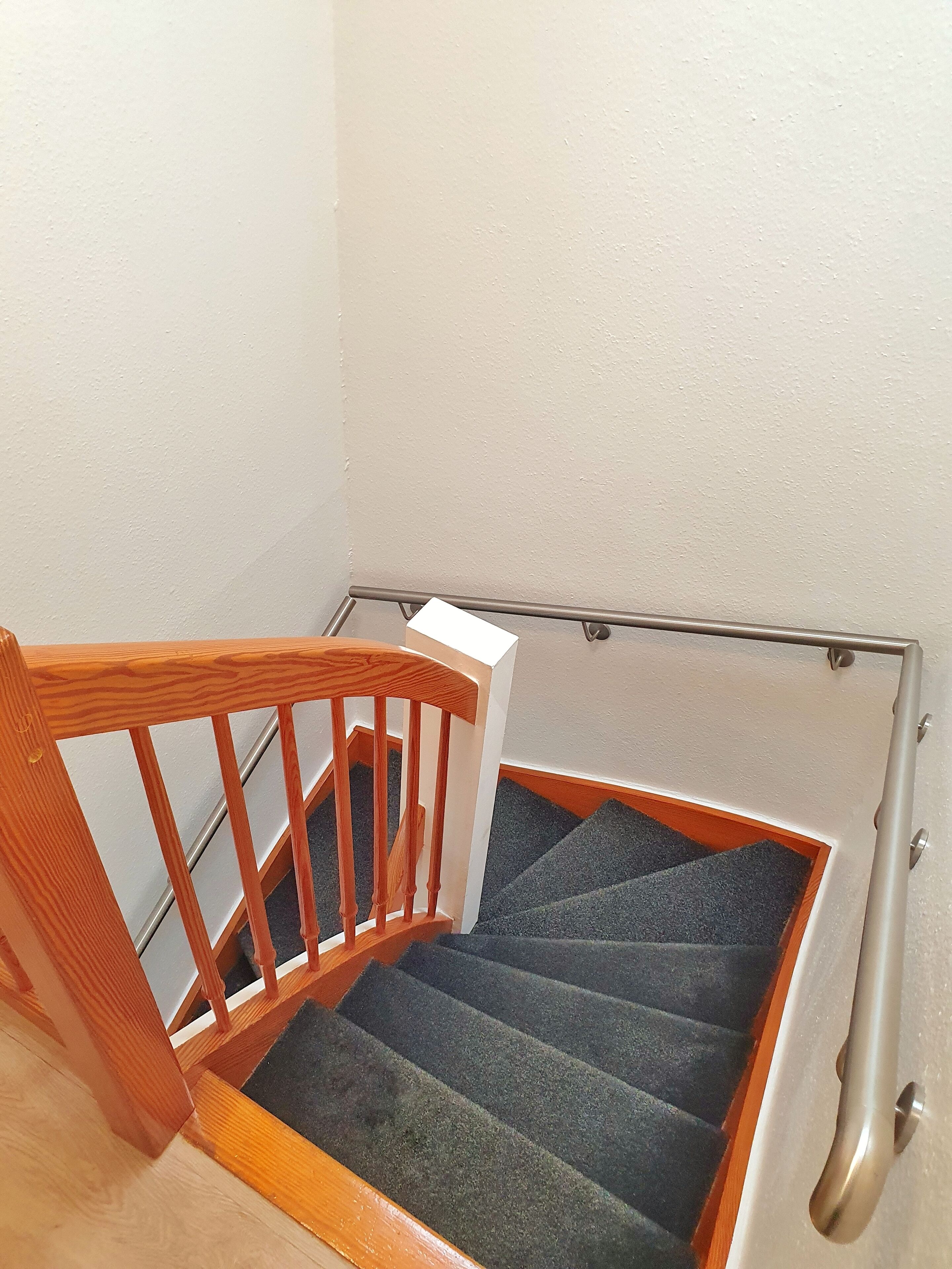A wooden staircase with a handrail and carpeted steps.
