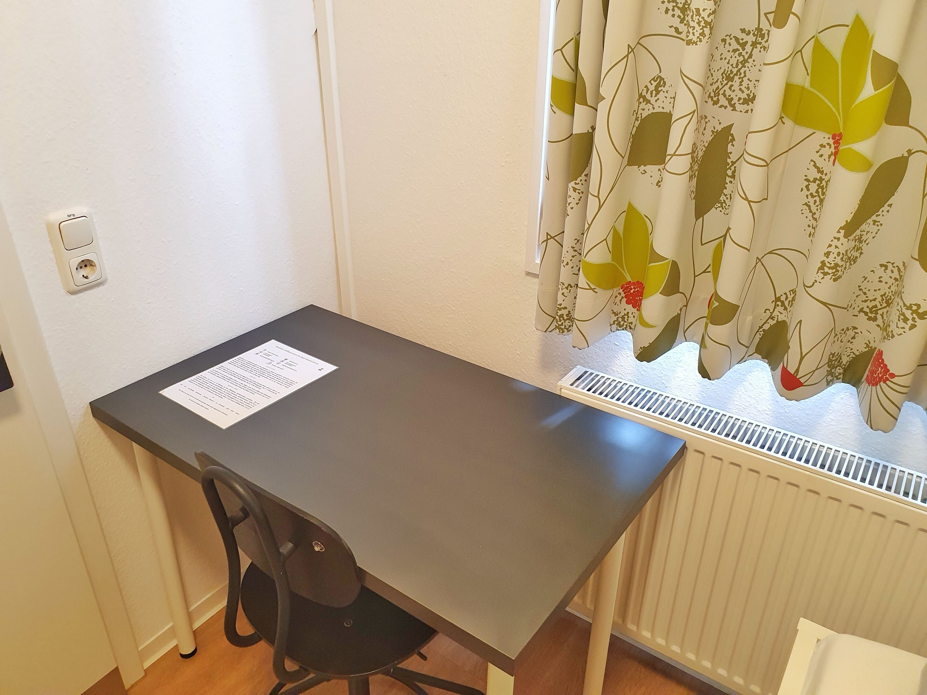 A small room with a desk, chair, and a radiator.
