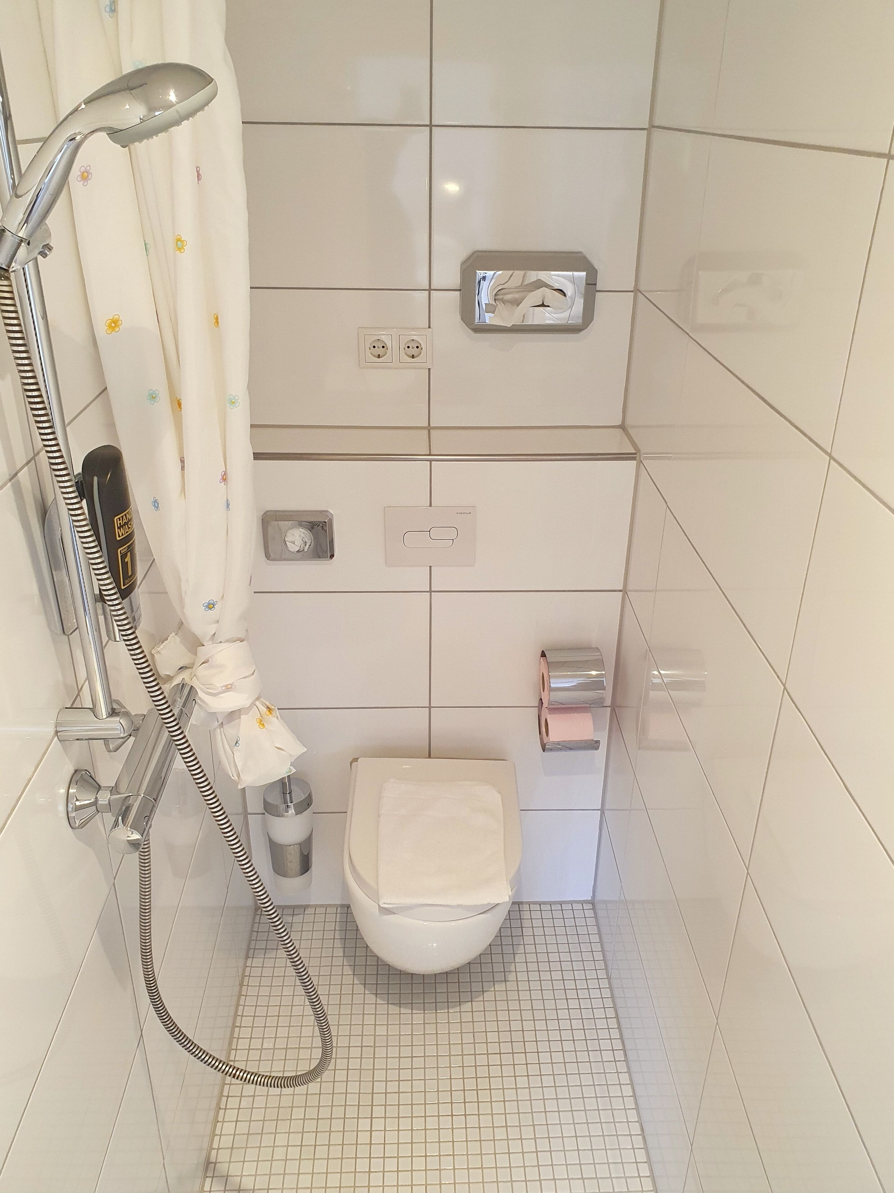 Ett badrum med dusch, toalett och en handduksställning.