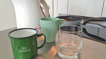 Un comptoir de cuisine avec une machine à café blanche, une tasse verte, un verre transparent et une poêle noire.
