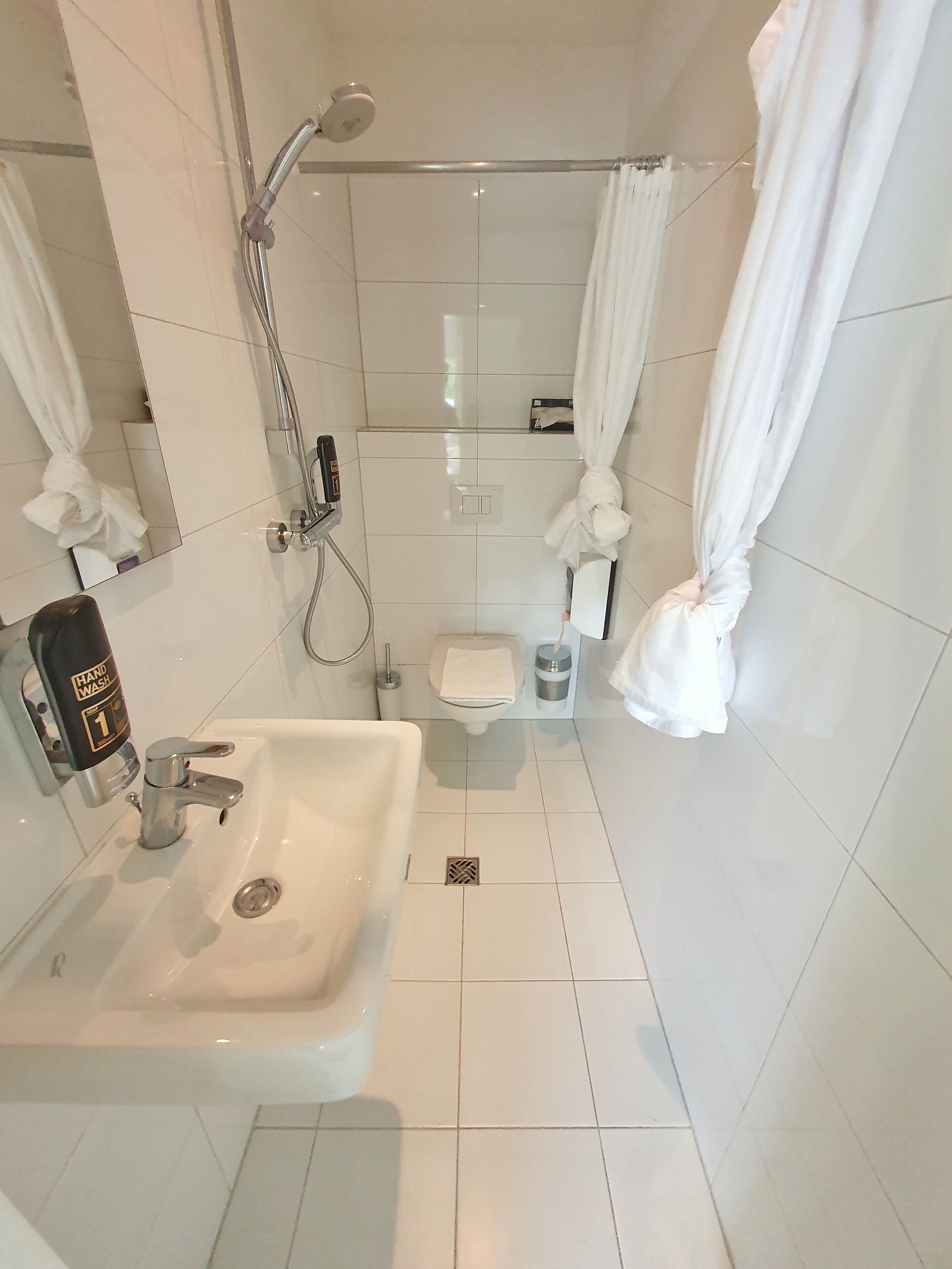 A bathroom with a white sink, a handheld showerhead, a toilet, and a shower curtain.