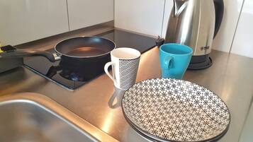 Ett kök med en spis, en stekpanna, en mugg, en blå mugg och en vattenkokare.