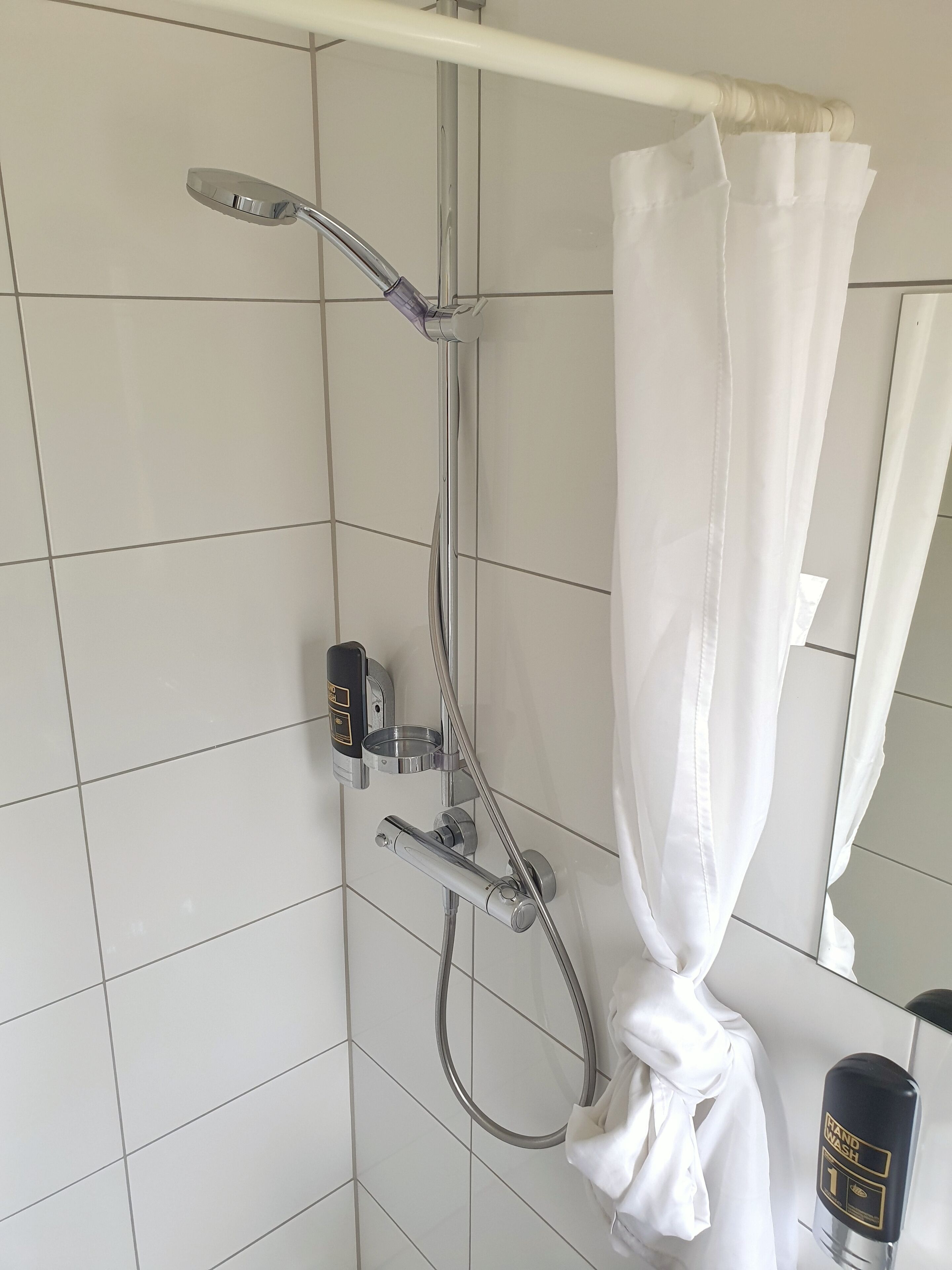 Een douchecel met douchekop en handdouche, plus bedieningspaneel.
