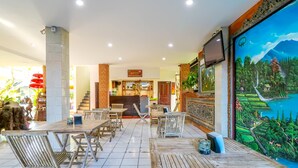 Un restaurant avec des tables et des chaises en bois, une fresque représentant un paysage et une enseigne au-dessus du comptoir.