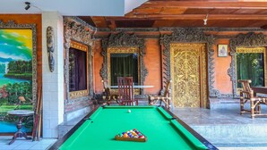Une table de billard avec des billes de couleurs vives, entourée de portes richement décorées et d’une fresque murale.