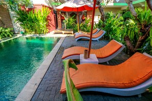 A poolside area with lounge chairs and umbrellas. - Capital O 1666 Grand Pudjawan Hotel Near Kuta Beach (Kuta)