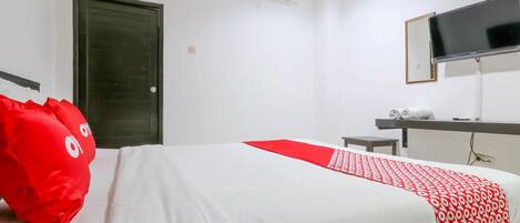 A hotel room with a bed, a TV mounted on the wall, a door, and an air conditioning unit.