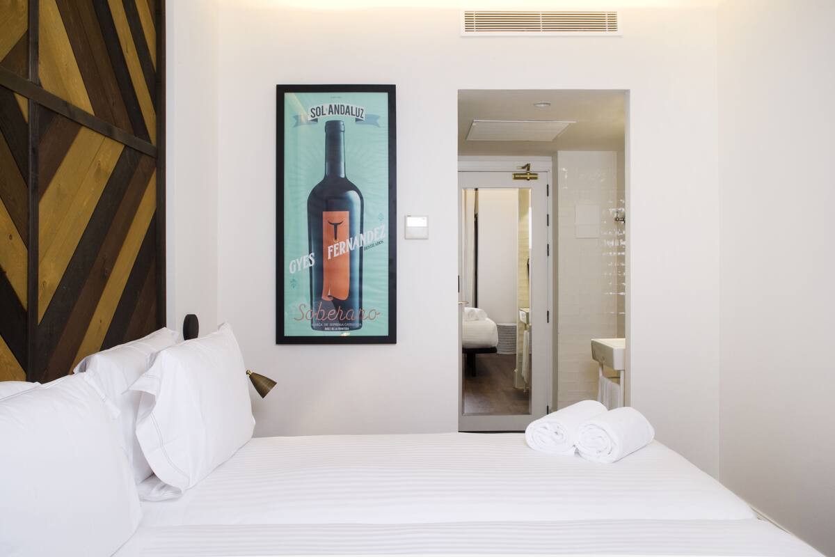 Une chambre d’hôtel avec un lit, du linge de lit blanc, une affiche encadrée au mur et une porte donnant sur une salle de bain.