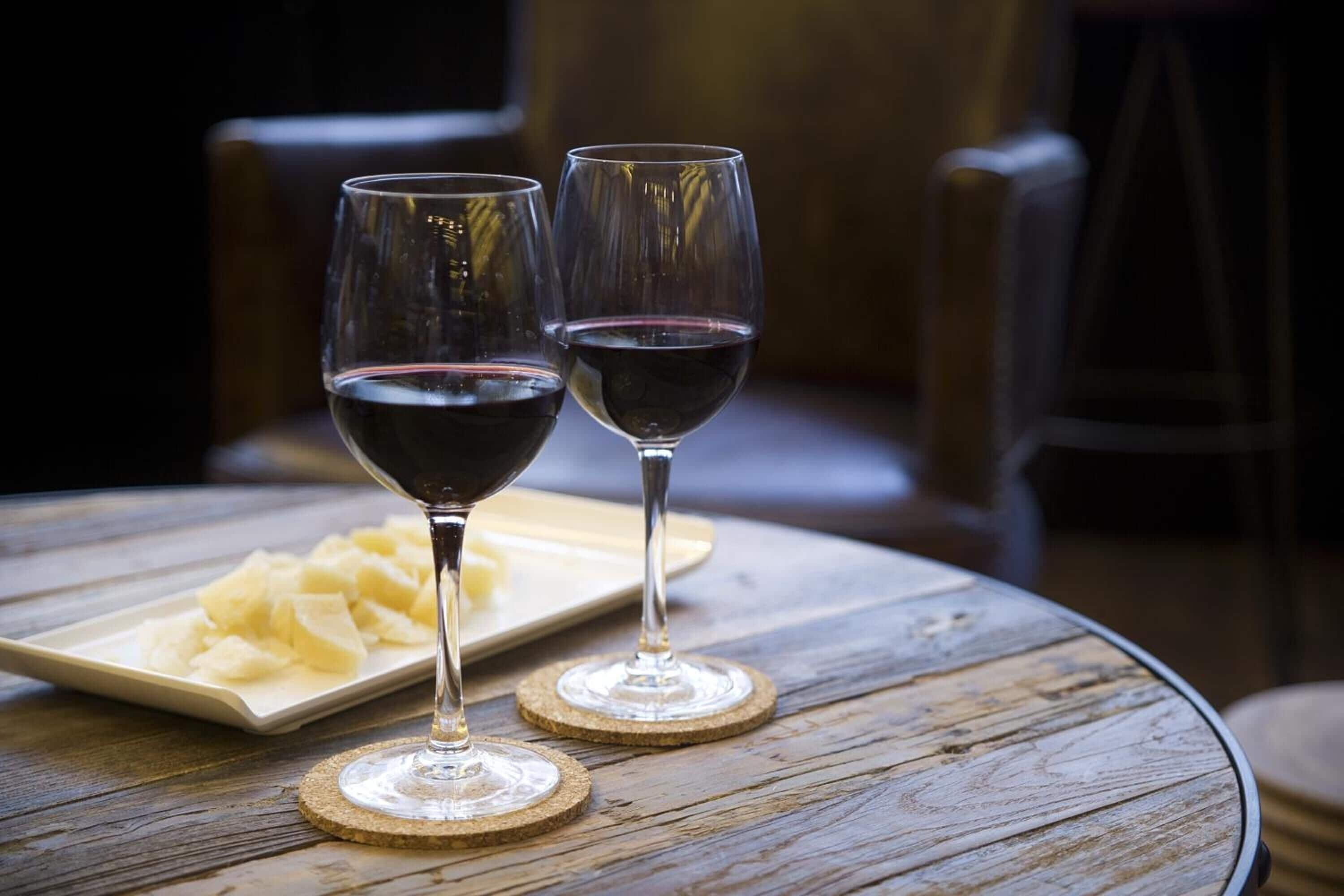 Deux verres à vin sont posés sur une table ronde en bois, à côté d’une assiette de fromage.