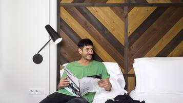 Una persona leyendo una revista en una cama en una habitación con un cabecero de madera con diseño en chevron y una lámpara de pie negra.