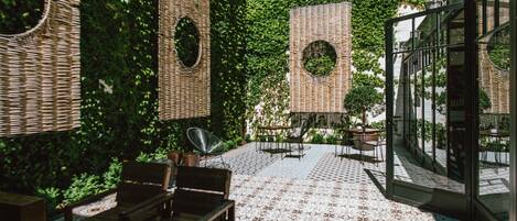 An outdoor patio with wicker furniture, a patterned floor, and a glass enclosure with a view of the greenery.